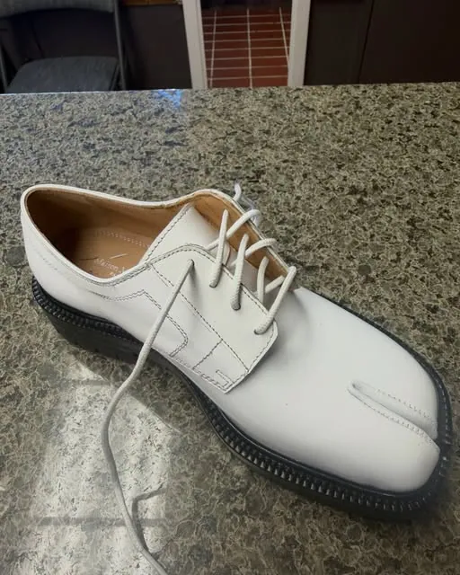 A white leather lace-up shoe with a new black sole and split toe