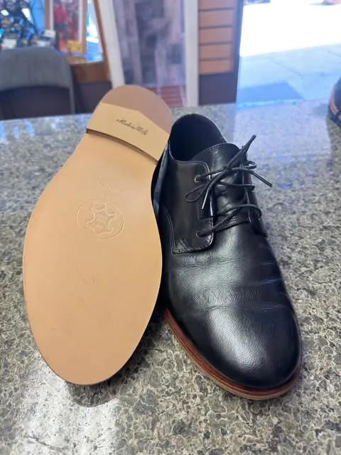 A black leather derby shoe next to the fresh tan leather sole fitted to its pair
