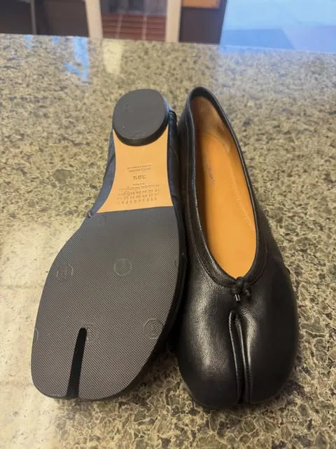 A pair of black Tabi flats, one turned over to show its new split-toe sole