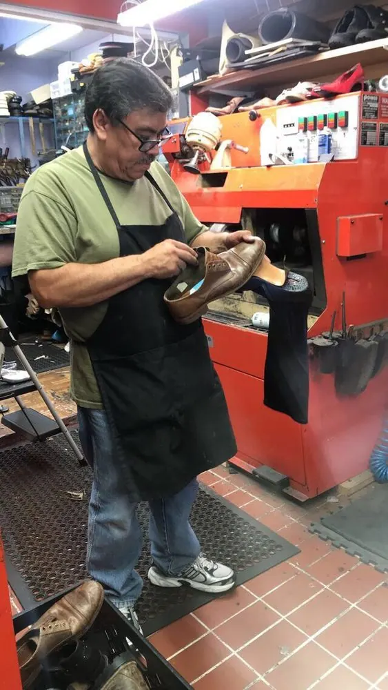 Marc at the bench in a work apron, inspecting a leather shoe