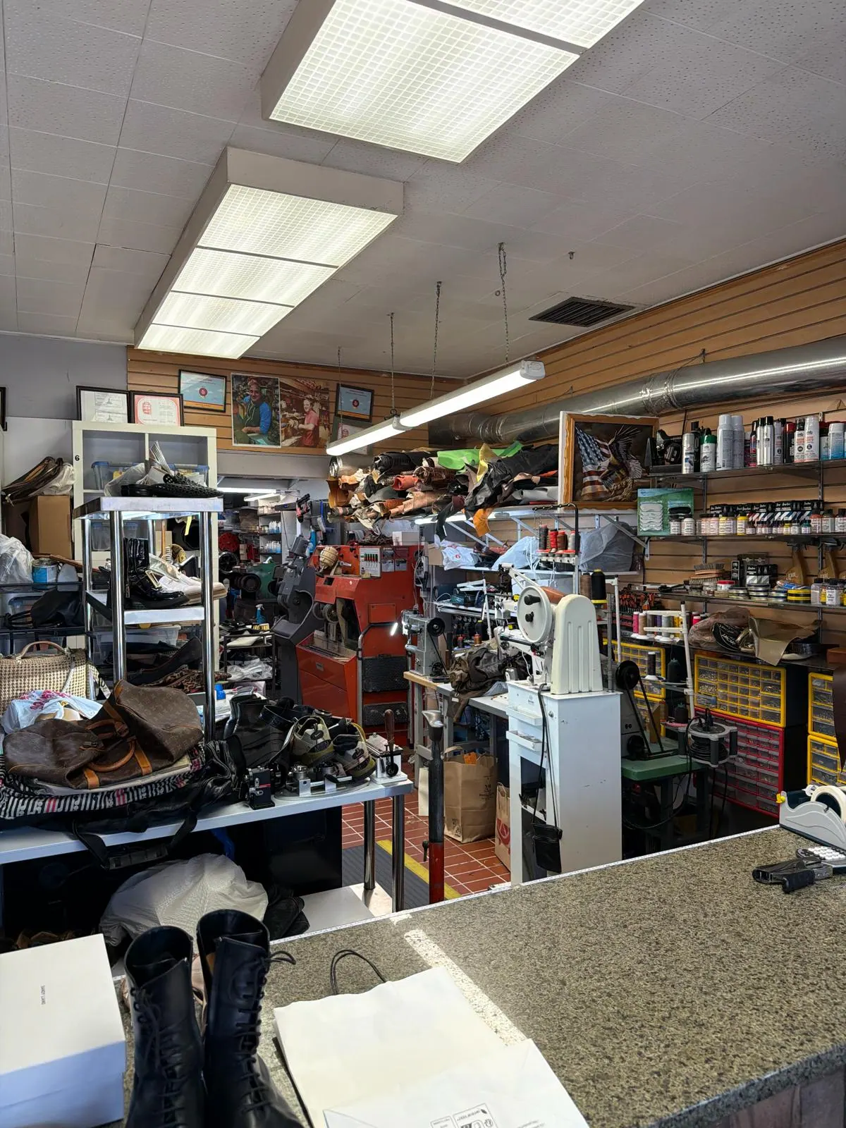 Inside Robert's Shoe Repair, looking past the counter: the red finishing machine, the stitchers and sewing machines, and hides of leather stacked on the shelves